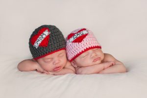 Five week old sleeping boy and girl fraternal twin newborn babies. They are wearing crocheted "Love Mom" and "Love Dad" beanies.